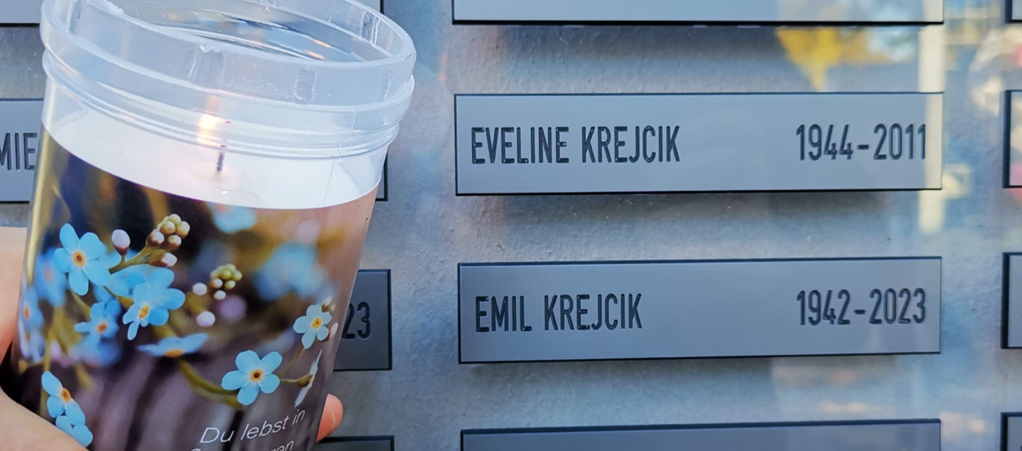Ein Gedenklicht mit Vergissmeinnicht vor den Namen Eveline und Emil Krejcik